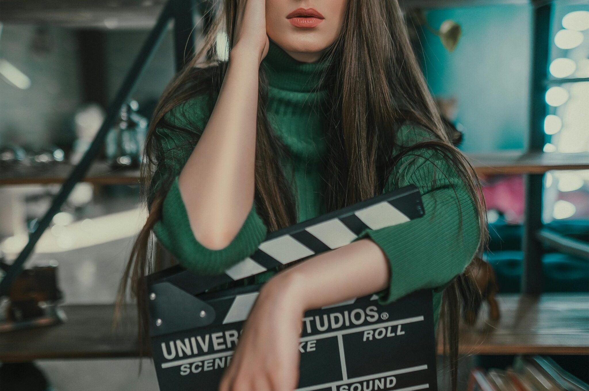 Striking portrait of a model with vibrant makeup and rainbow socks holding a clapperboard indoors.